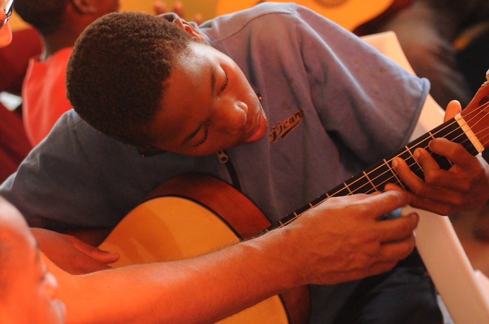 a student eagerly learning how to properly place his fingertips on the guitar strings